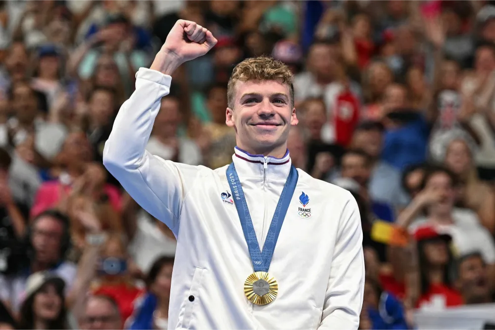 Léon Marchand célèbre sa victoire aux Jeux Olympiques de Paris 2024 avec une médaille d'or autour du cou, symbole de son ascension fulgurante en natation.